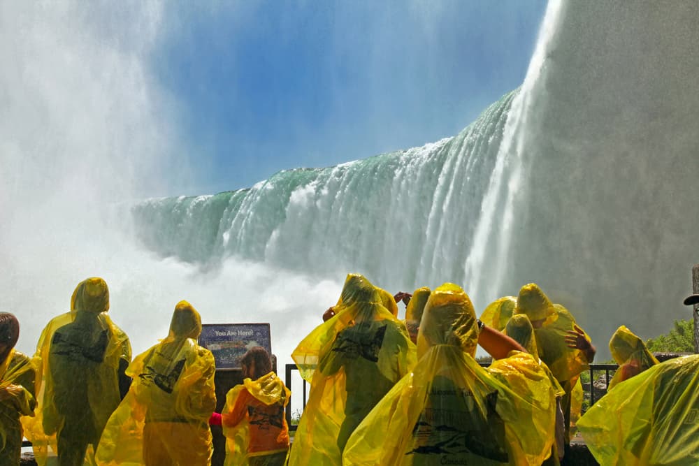 Group of people standing near niagara falls wearing yellow raincoats