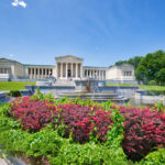 A museum in Buffalo, New York with a fountain and colorful rose bushes on a sunny day