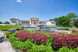 A museum in Buffalo, New York with a fountain and colorful rose bushes on a sunny day