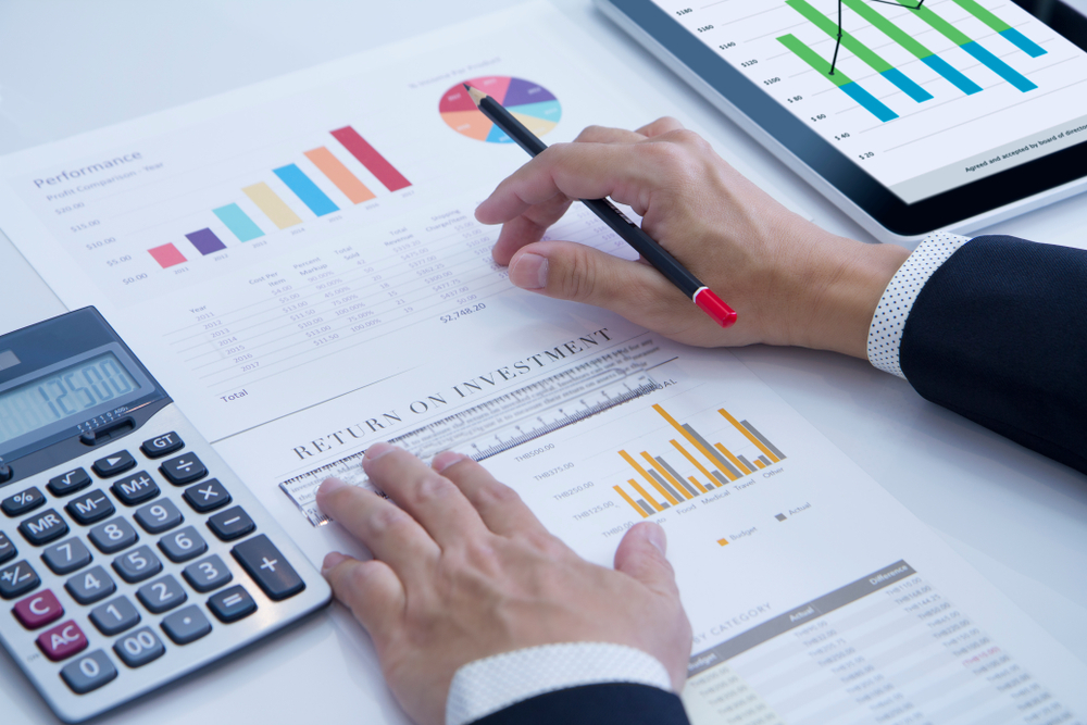 A man in a suit calculates the ROI of his residential rental property with graphs and a calculator